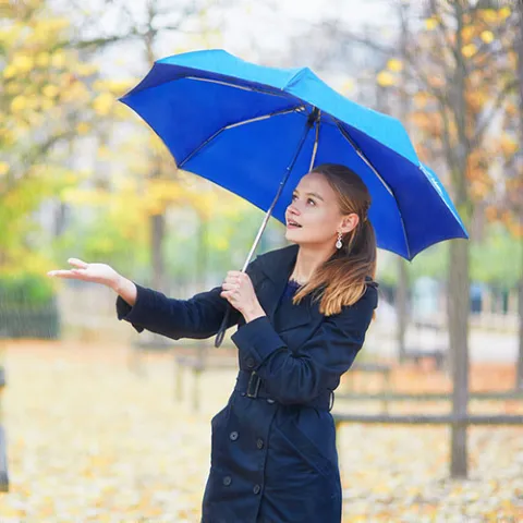 Woman holding a blue umbrella in autumn